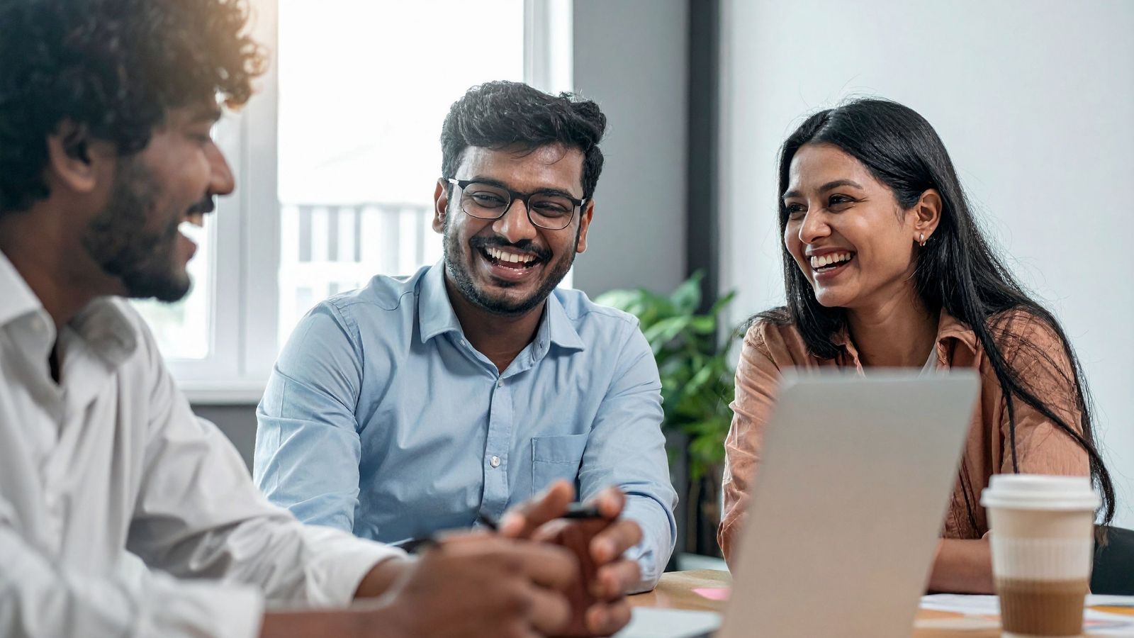 Indian professionals in discussion around a laptop in a bright office