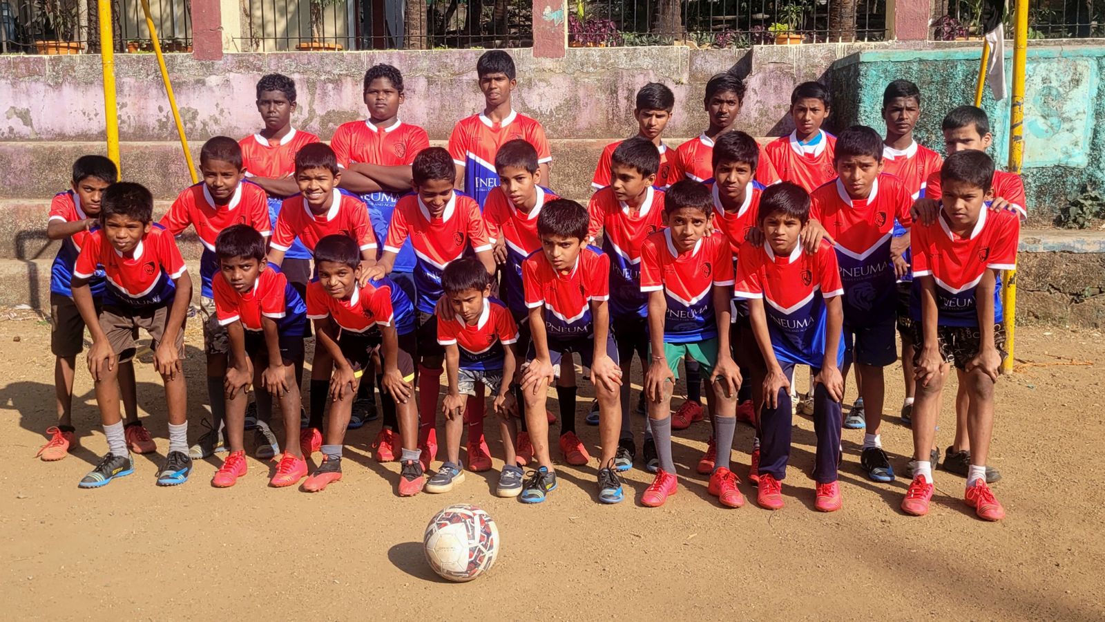 Pneuma FC youth squad in red and blue kits posing with a football on a practice ground